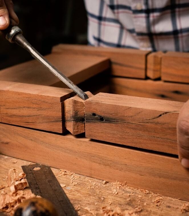 Focused view of a person skillfully using a chisel on wooden pieces indoors.